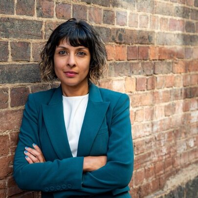 Woman standing with arms folded next to a brick laneway.