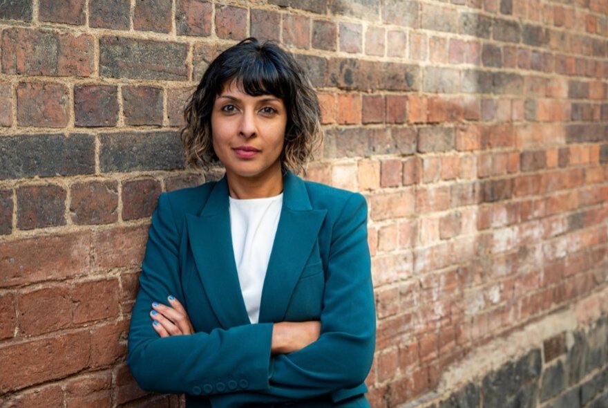 Woman standing with arms folded next to a brick laneway.