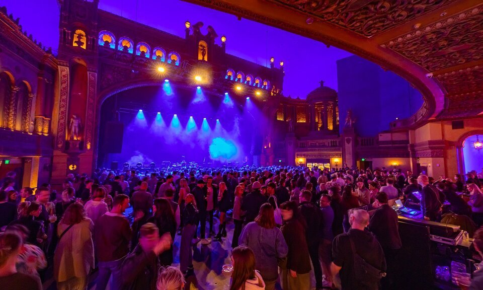 A stage with a grand facade to look like a building, with crowds waiting for a band to come on stage.