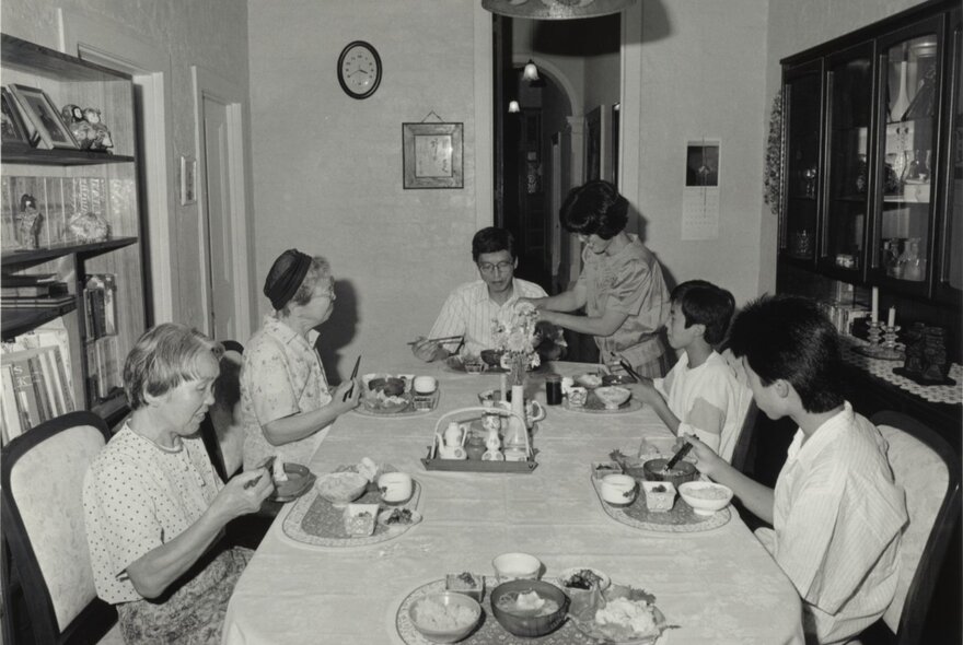 A black and white photograph of a family eating a meal at the family dining table circa 1950.