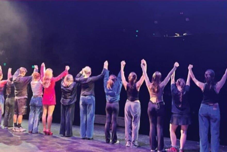 Stage show cast standing with arms raised on stage at the end of a show.
