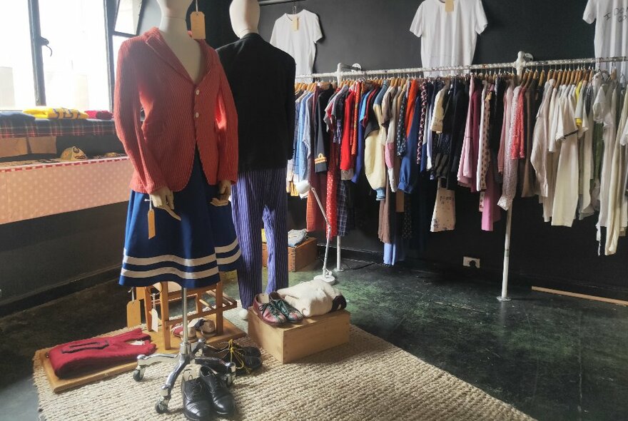 A rack of clothing inside a small studio space, with two mannequins dressed in vintage clothes in the middle of the room. 