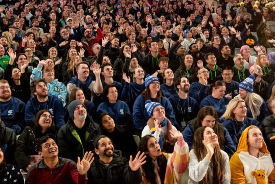 A large crowd of people all together looking upwards and smiling in warm clothing.