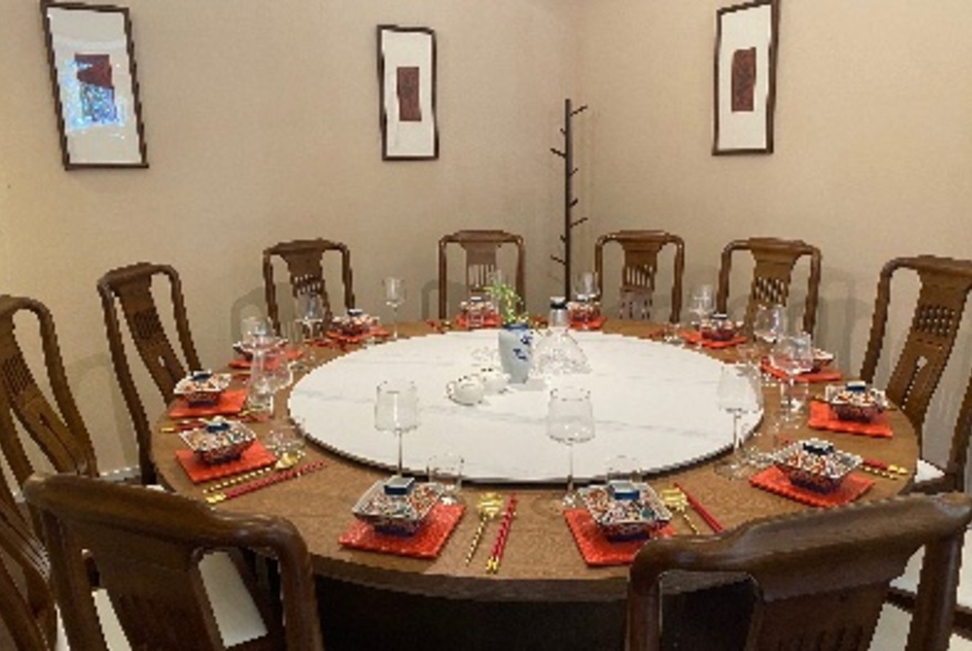 A large round table in the corner of a restaurant with a lazy susan, tall brown chairs and set with traditional Chinese crockery.