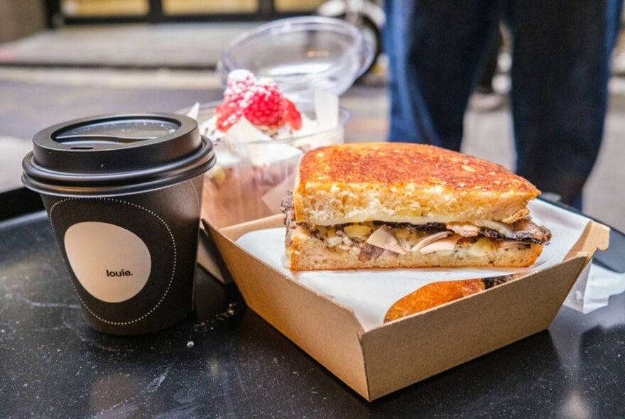 Takeaway coffee cup on a table next to a toasted sandwich.