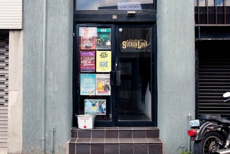 Entrance to club, with black doorway, posters on glass to left.