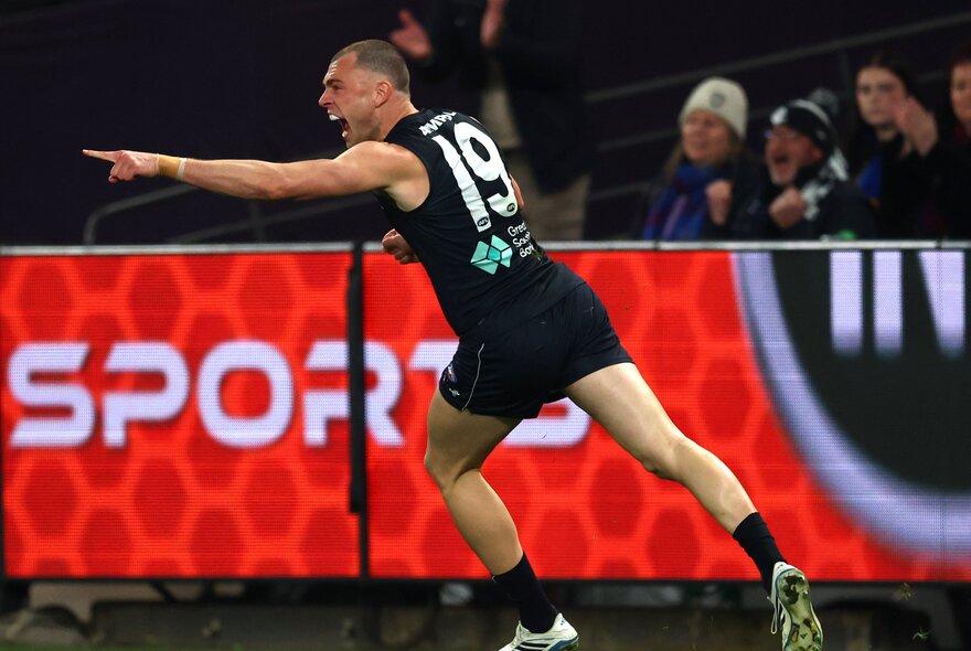 A Carlton Blues AFL player pointing in celebration during a game.