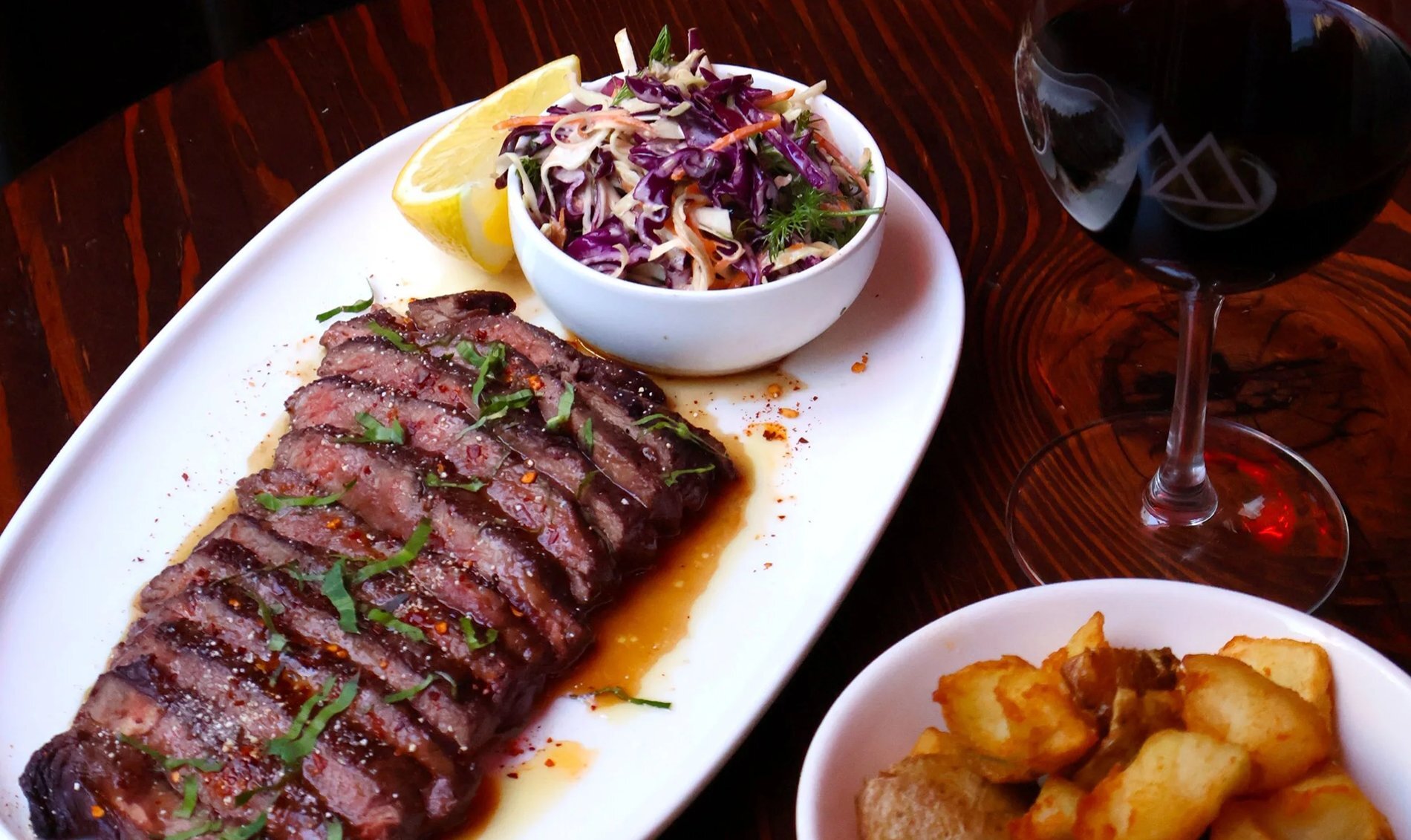 A plate of sliced steak with salad, potatoes and red wine.