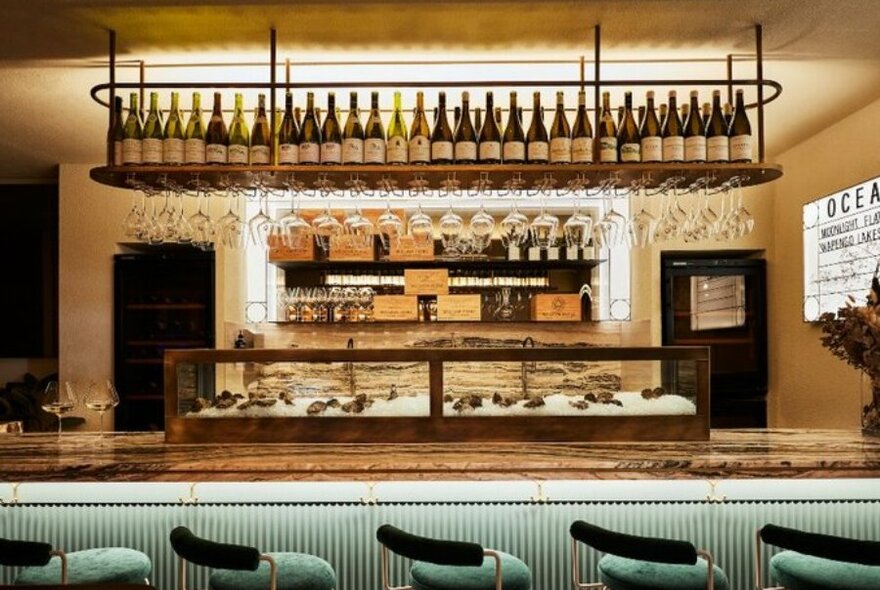 A bar with blue velvet stools, wine bottles and a large oyster display cabinet.