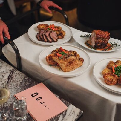 A Dolly food trolley being wheeled by a waiter, with plates of roast meats and vegetables.