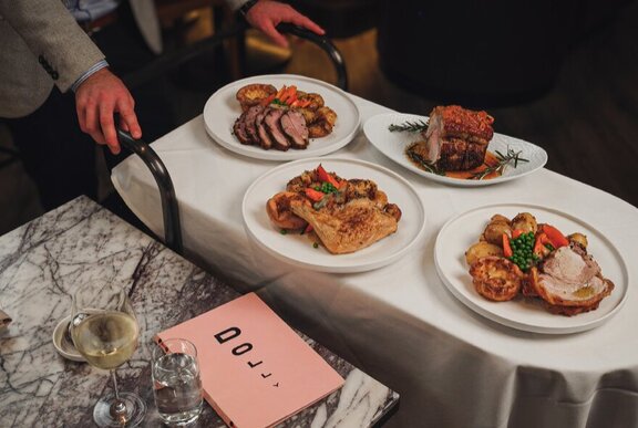 A Dolly food trolley being wheeled by a waiter, with plates of roast meats and vegetables.