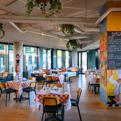 The interior of an Italian restaurant with red and white checked tablecloths and a column painted with an Italian chef holding up the specials menu.