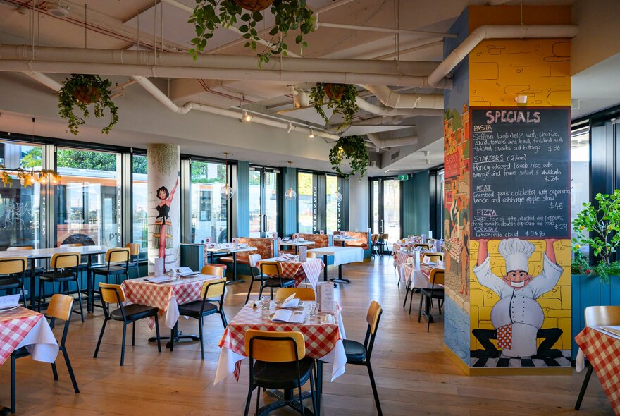 The interior of an Italian restaurant with red and white checked tablecloths and a column painted with an Italian chef holding up the specials menu.