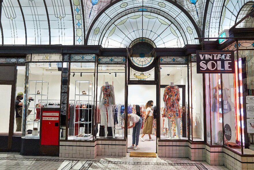 People shopping in a retail boutique with beautiful stained glass windows above.