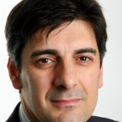 Close up of the face of George Megalogenis; a middle-aged man with short dark hair, dark eyes and a serious gaze.