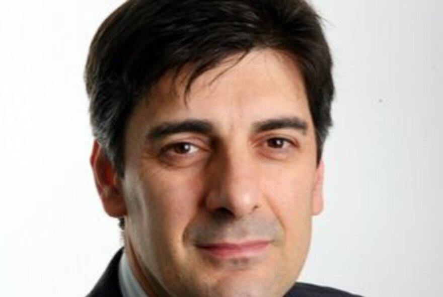Close up of the face of George Megalogenis; a middle-aged man with short dark hair, dark eyes and a serious gaze.