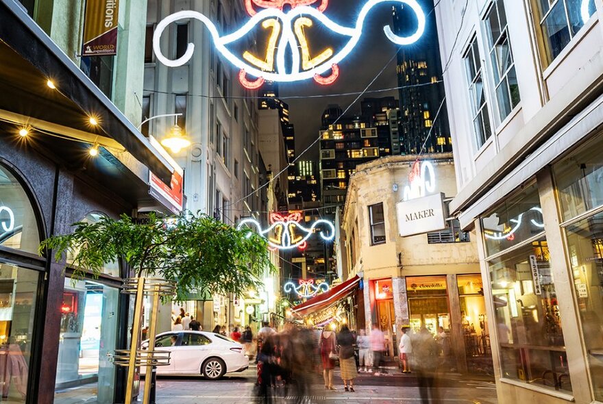 Light-up bell decorations hang over a laneway filled with people