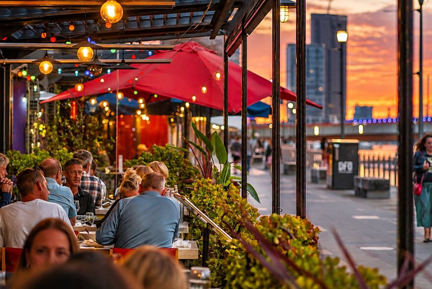 A view of the outdoor seating area at a restaurant in Melbourne, the sunset in the distance behind them.