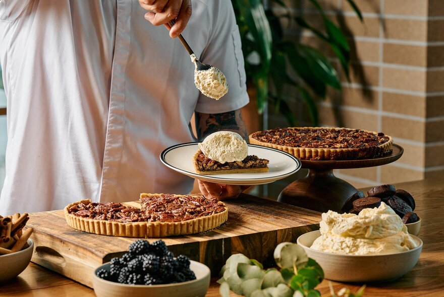 A person serving themselves a big dollop of cream on top of a slice of Southern-style pie on a plate, in front of the dessert display at a restaurant. 