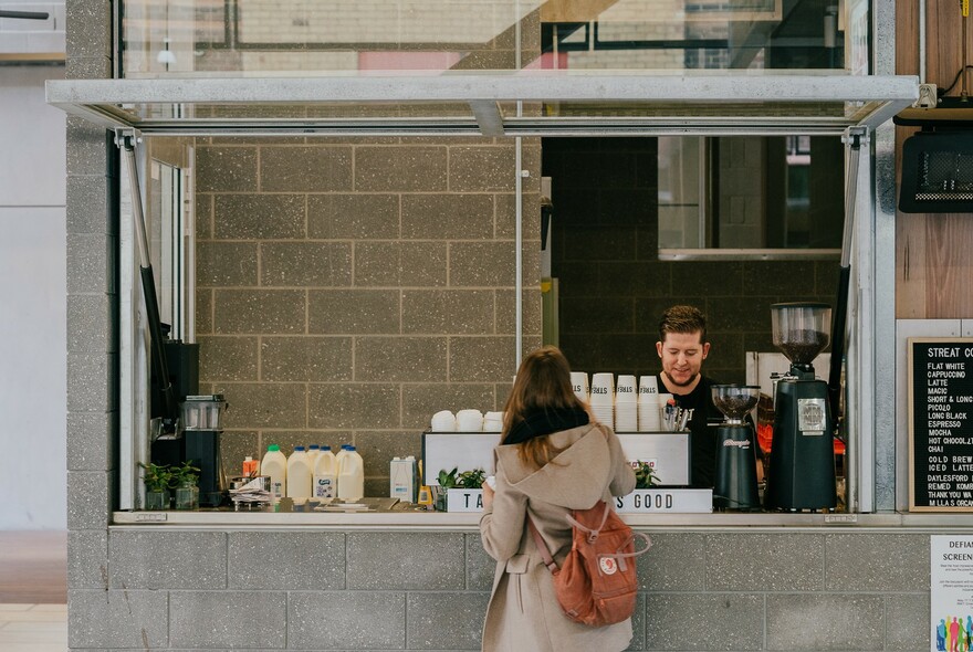 Customer standing at a hole-in-the-wall takeaway coffee vendor.