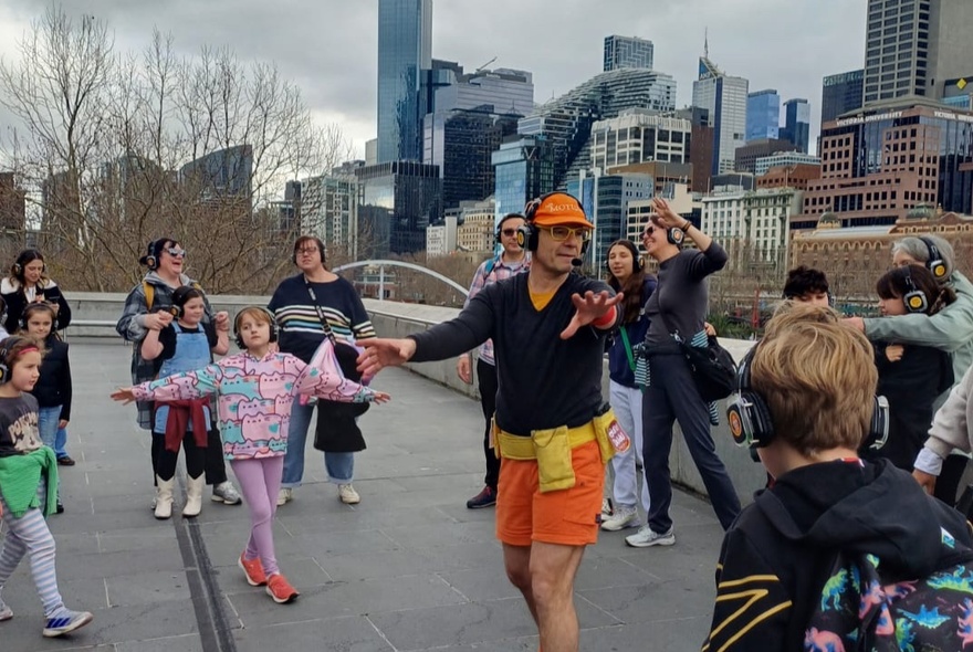 Dance tour leader with kids dancing on a rooftop with city buildings.