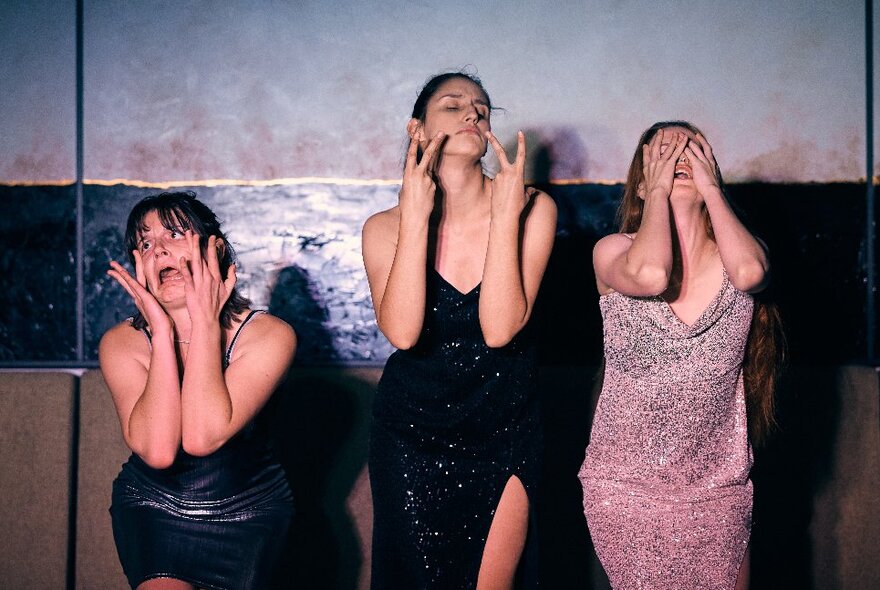 Three women in evening dresses with hands to their face in exaggerated poses.