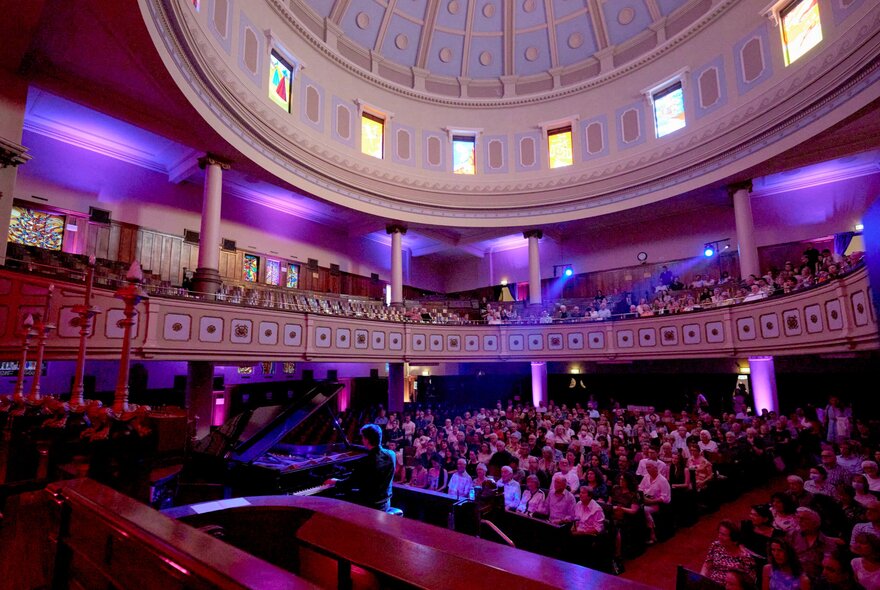 The interior of the Toorak Synagogue, showing the domed ceiling and a large seated audience for a piano recital.