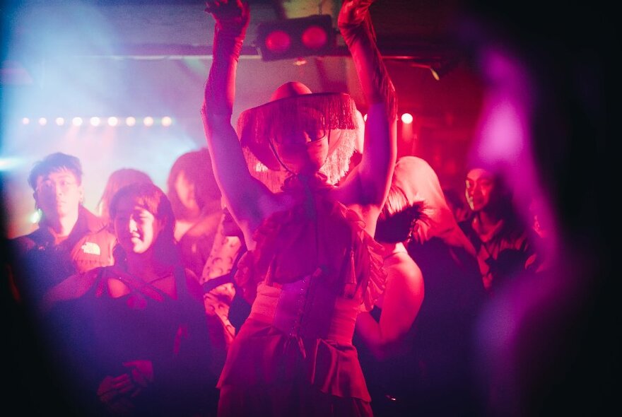 People dancing and smiling in a nightclub, with coloured lights casting a pinkish glow over the scene.