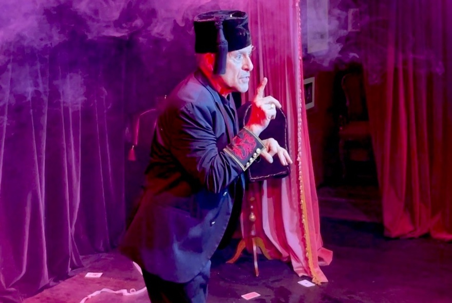 A man performing a magic show on stage, wearing a Fez.