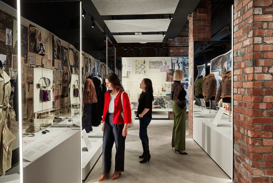 Three women walking through an exhibition showcasing military clothing.