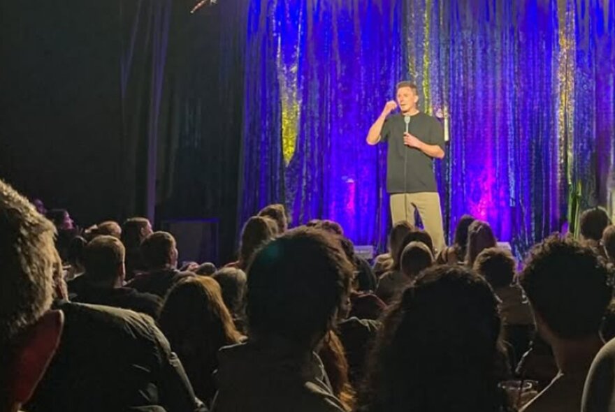 A stand up comedian on stage performing in front of an audience.