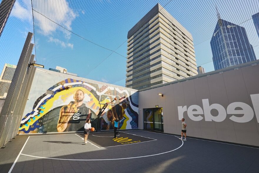 An outdoor basketball court at Rebel Emporium in the Melbourne CBD, with kids playing and large mural. 