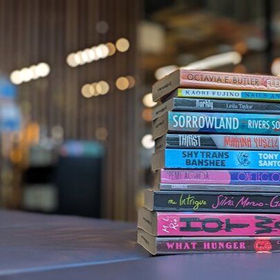 A vertical stack of books spine facing out, on a table inside a library.