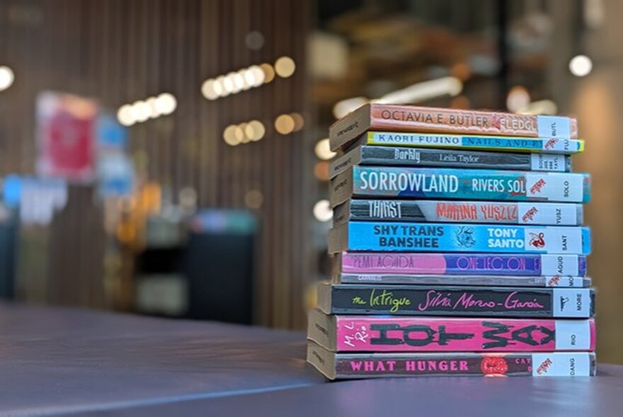 A vertical stack of books spine facing out, on a table inside a library.