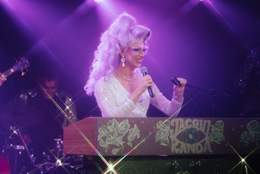 A drag queen with big hair performing on stage with purple lighting. 