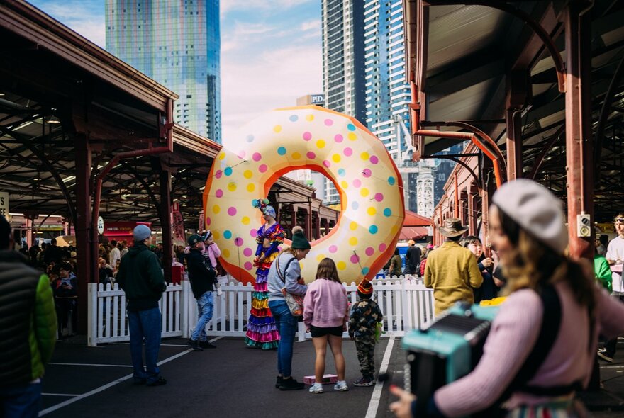 Looking down an alley in the Queen Victoria Market with a small white picket fence and a giant inflatable donut with sprinkles.