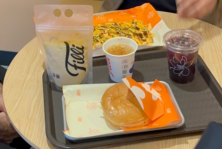A donut, chai tea in a plastic sleeve and two drinks on a grey plastic tray.
