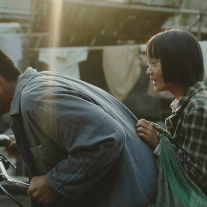 A scene from the film A Foggy Tale showing a man riding a bicycle with a girl seated on the bike behind him as a passenger.