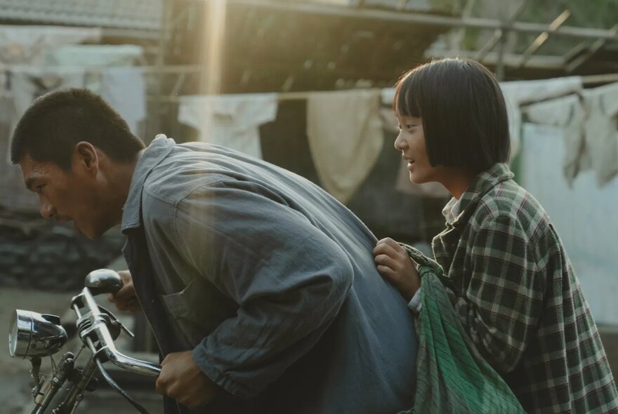 A scene from the film A Foggy Tale showing a man riding a bicycle with a girl seated on the bike behind him as a passenger.