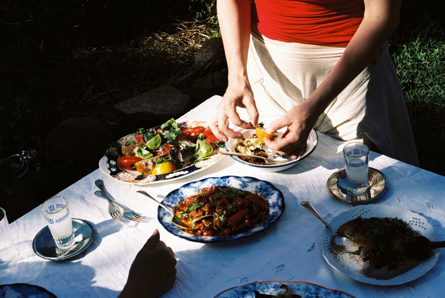 Hands tearing up ingredients that are going into plates of food at an outdoor table in part shade. 