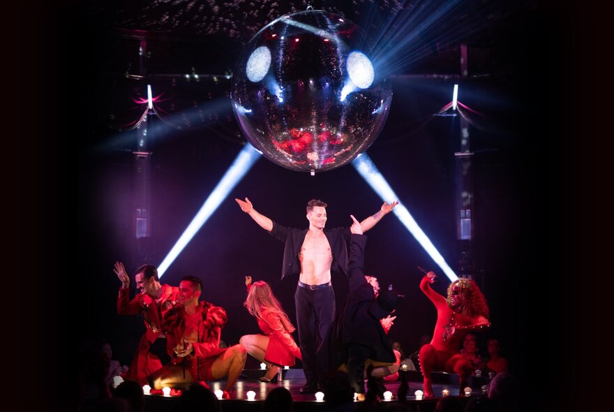 A circus performer in black leggings and a black shirt with his arms outstretched on stage.