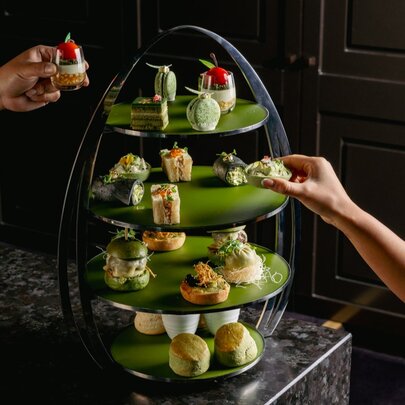 A matcha-themed green high tea with a 4-tiered tray or treats and hands reaching out to take treats. 
