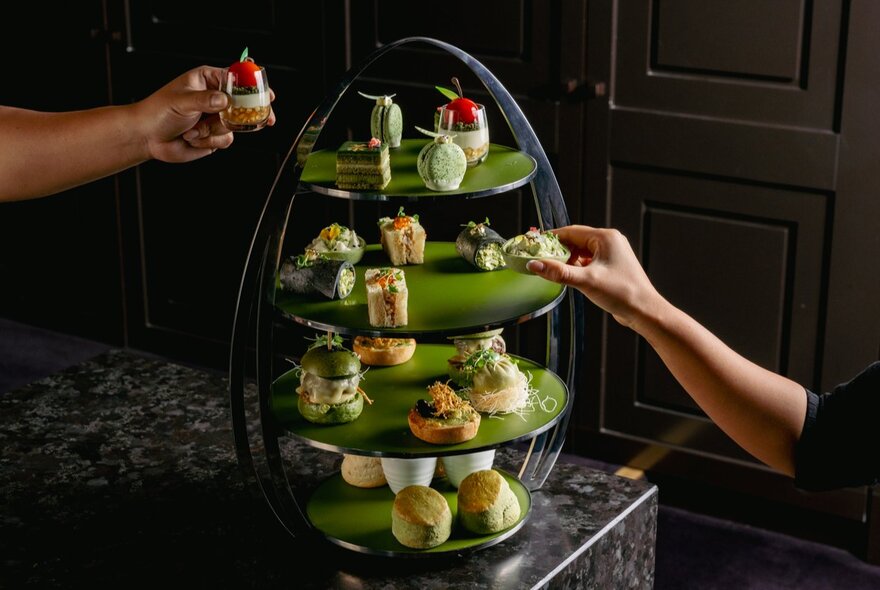 A matcha-themed green high tea with a 4-tiered tray or treats and hands reaching out to take treats. 