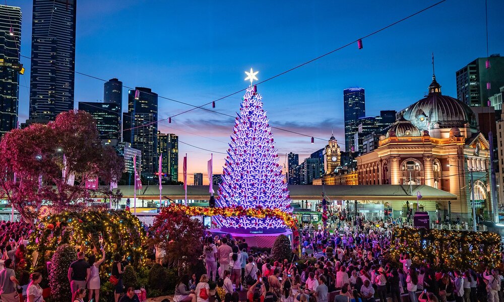 A Christmas tree lit up in the city with crowds around.