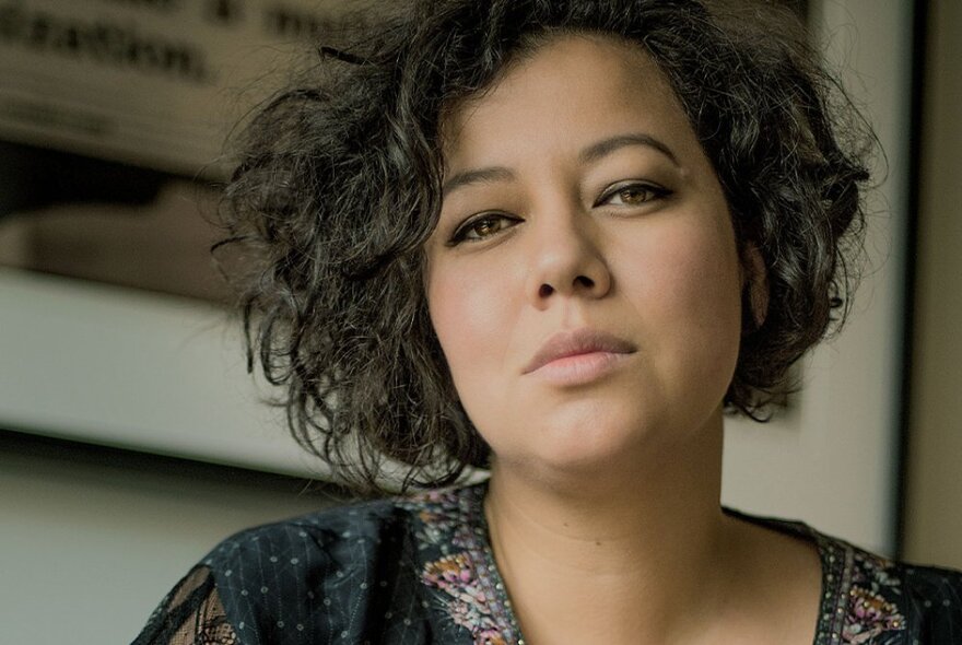 Singer Mahalia Barnes, looking downwards with short unruly hair, wearing a dark embroidered top.