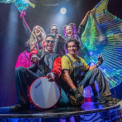 Five children's circus performers on stage in colourful costumes.