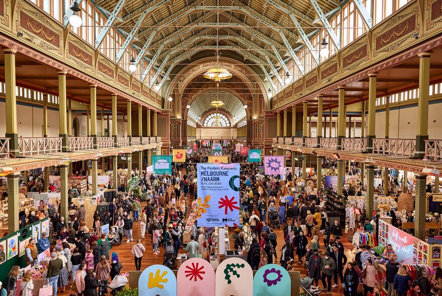 A busy market in the Royal Exhibition Building with large colourful banners.