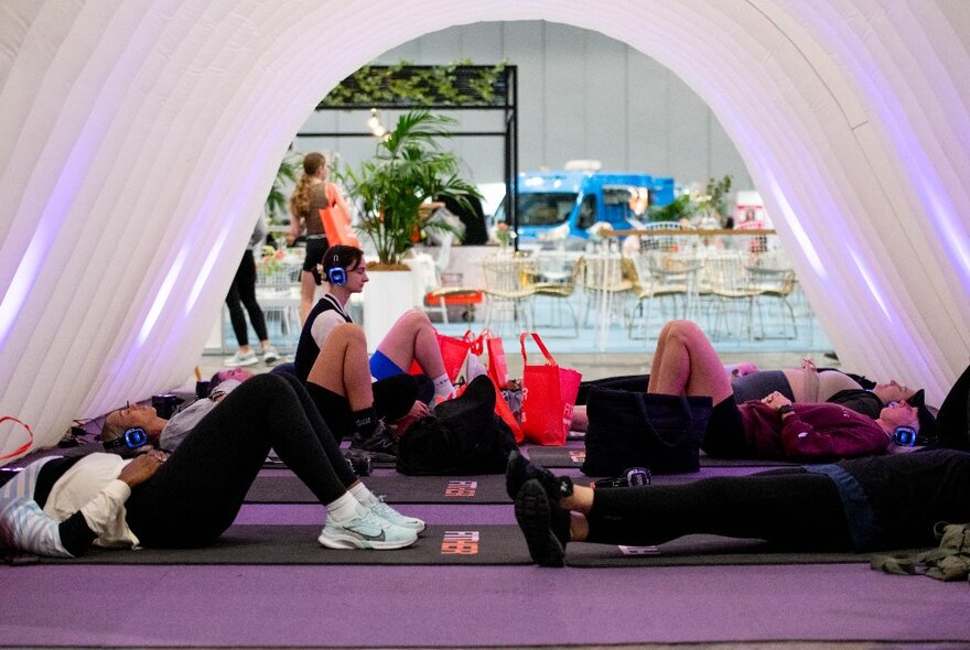 A group of people lying on the floor under a tent doing exercises.