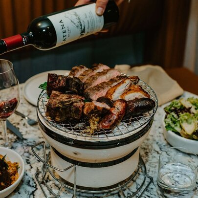 A large plate of meat next to a glass of wine and other dishes.