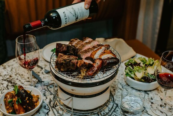 A large plate of meat next to a glass of wine and other dishes.